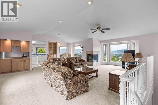 Living room and dining area with fireplace, large windows showing a valley view, and kitchen entrance. - 695 Valley Road, Kelowna