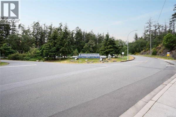 Roadway intersection near a sign for Thetis Lake Park surrounded by trees and a hill. - 696 Madrona Ridge, Langford