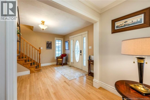 Wide view of a spacious foyer with wood floors, a staircase, and a view of the front entrance. - 698 Frampton, Moncton