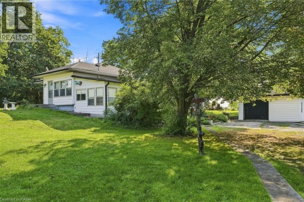 View of a grassy yard with mature trees, a driveway, and a garage. - 698 York Road, Dundas