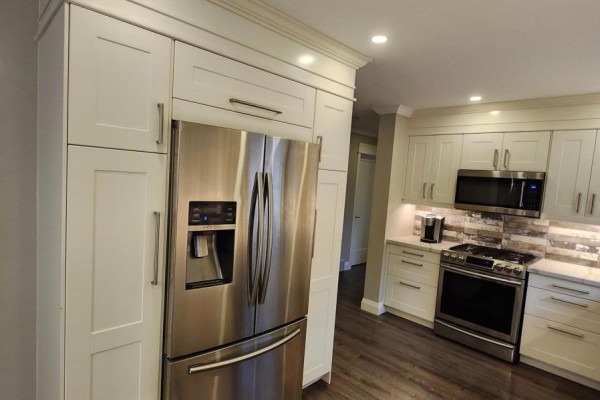 Stainless steel refrigerator with ice dispenser next to cream cabinets in a modern kitchen. - 699 Castleguard Crescent, Burlington