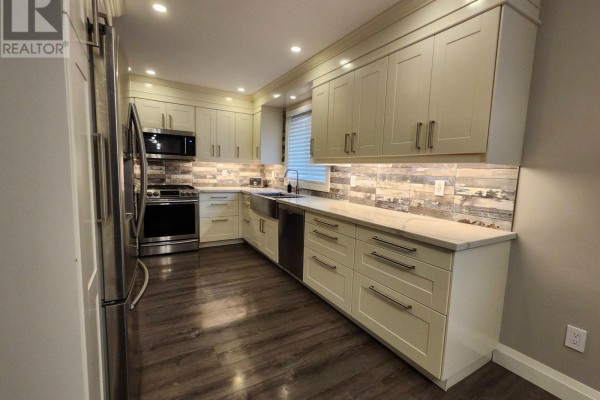 L-shaped kitchen featuring cream cabinets, stainless steel appliances, farmhouse sink, and dark wood flooring. - 699 Castleguard Crescent, Burlington