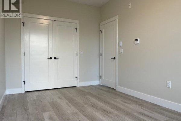 Empty room with light grey walls, wood-look flooring, and two white double doors. - 6xx 22638 119 Ave, Maple Ridge