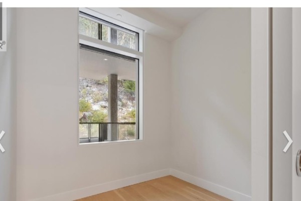 Empty white room with a single window showing a rock face and trees. - 6xx 6687 Nelson Avenue, West Vancouver