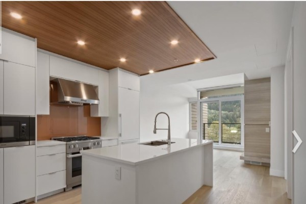 Modern white kitchen with stainless steel appliances, a large island, and a wood-paneled ceiling. - 6xx 6687 Nelson Avenue, West Vancouver