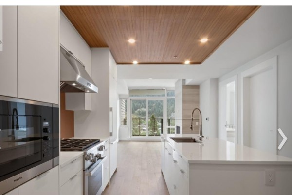 Contemporary kitchen and living area with white cabinets, island, and a view of trees and mountains. - 6xx 6687 Nelson Avenue, West Vancouver