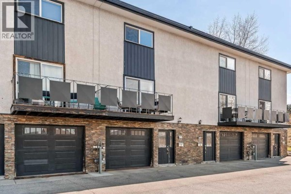 Living room with view of balcony through sliding glass doors, dark wood floors, and bookshelf. - 7, 1603 Mcgonigal Drive Ne, Calgary