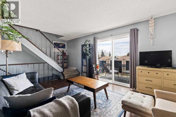 Balcony with outdoor seating and table, metal railings, and string lights, overlooking townhouses. - 7, 1603 Mcgonigal Drive Ne, Calgary