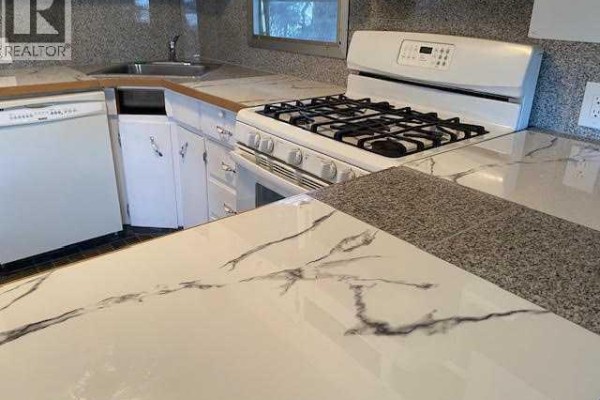 Close-up of a white gas range and marble countertop in a kitchen. - 7, 726 Carmichael Lane, Hinton