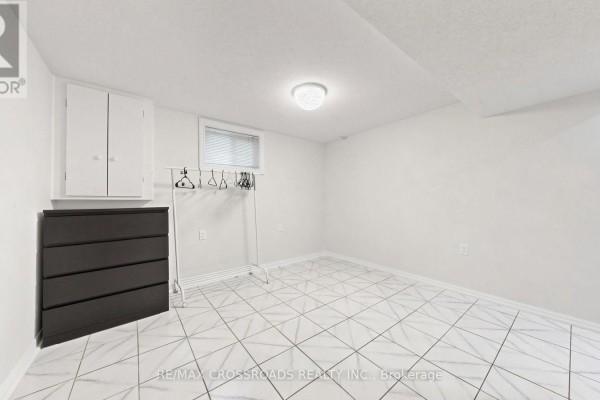 Basement room with white walls, white tiled floor, dresser, and clothing rack. - 7 - 106 Stilecroft Drive, Toronto