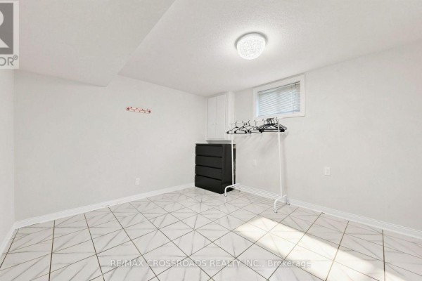 Empty basement room with white walls, white tiled floor, and a dresser. - 7 - 106 Stilecroft Drive, Toronto