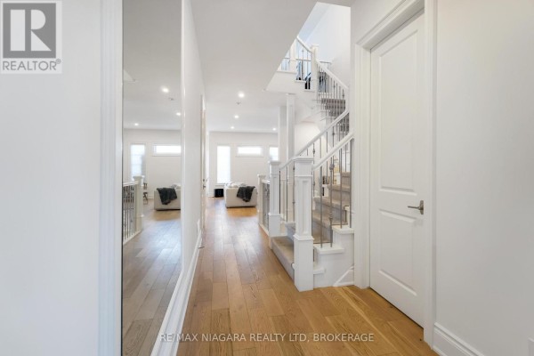 Hallway facing living area with hardwood floors and white staircase. - 7 - 15 Arbourvale Common Road, St  Catharines