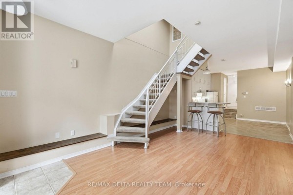 Living room with a staircase, island kitchen with bar stools, and wood laminate flooring. - 7 - 170 Cathcart Street, Ottawa