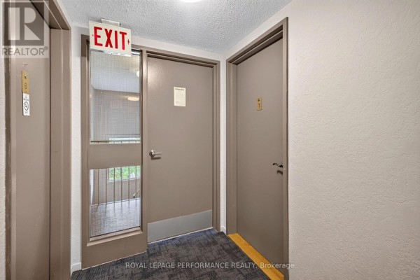 Interior hallway with beige doors, a red EXIT sign, and textured carpet. - 7 - 18 Sweetbriar Circle, Ottawa