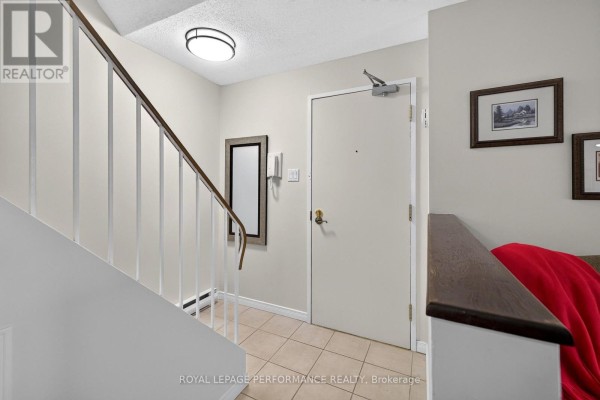 Interior hallway with a beige door, framed artwork, and a white staircase railing. - 7 - 18 Sweetbriar Circle, Ottawa