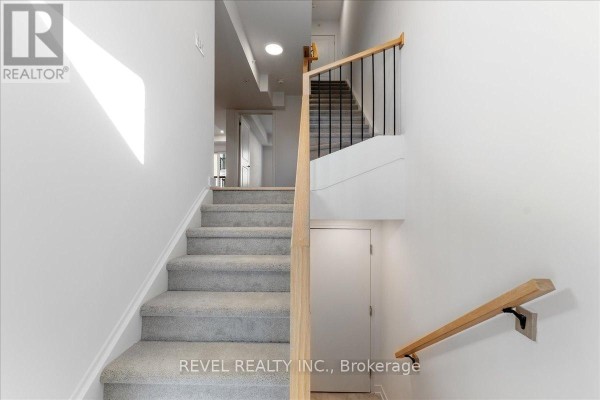 Staircase inside a townhouse with white walls, gray carpet, and wooden banister. - 7 - 200 Railway Engine House Way, Whitby