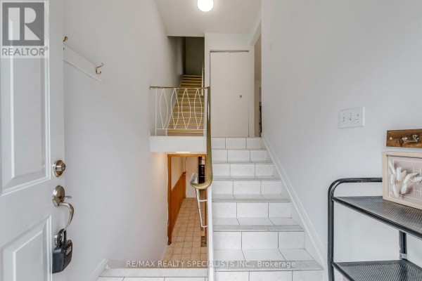 Interior foyer with white walls, white tiled stairs, a metal railing, and a door leading downstairs. - 7 - 325 Mary Street, Hamilton