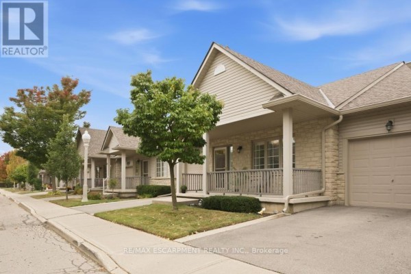 Exterior view of beige townhouses with covered porches and stone accents on a sunny day. - 7 - 34 Southbrook Drive, Hamilton