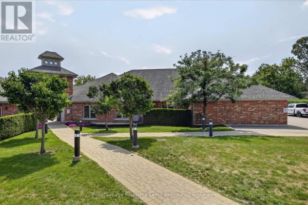 Side exterior view of brick townhouse complex with arched entrance and landscaping. - 7 - 35 Green Arbour Way, Kawartha Lakes