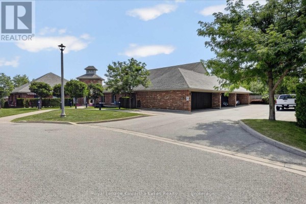 Street view of brick townhouse complex with garages and parking area. - 7 - 35 Green Arbour Way, Kawartha Lakes