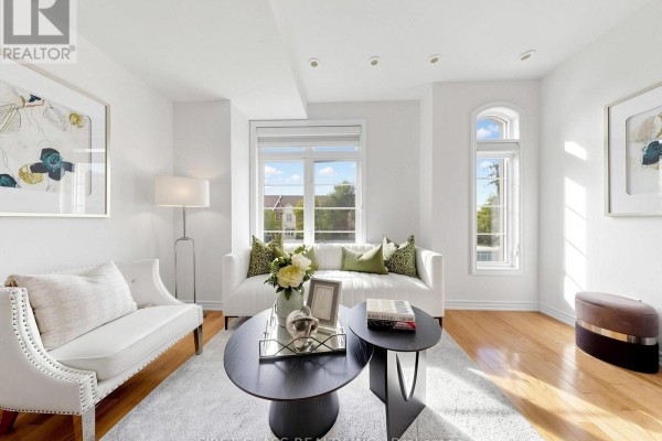 Living room with white sofas, wood floors, two dark oval coffee tables, and artwork on white walls. - 7 - 37 Drewry Avenue, Toronto