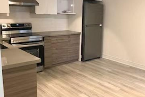 Corner view of the kitchen with wood-look flooring, grey countertops, stainless steel appliances, and white cabinetry. - 7 - 373 Broadview Avenue, Toronto