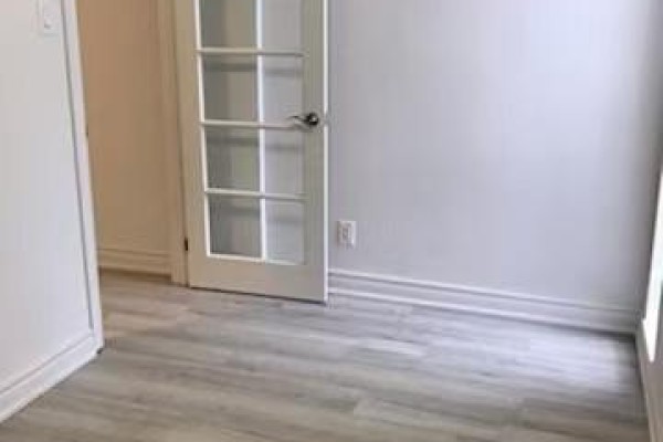 Empty room with light grey wood-look flooring, white walls, and a glass-paned door on the left. - 7 - 373 Broadview Avenue, Toronto