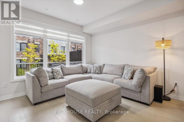Living room with a large sectional sofa, ottoman, and a floor lamp. - 7 - 40 Baynes Way, Bradford West Gwillimbury