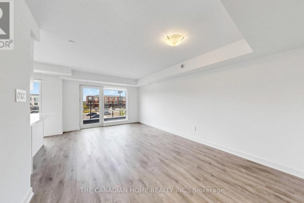 Empty living room with white walls, grey wood-look flooring, and large sliding glass doors. - 7 - 45 Romilly Avenue, Brampton