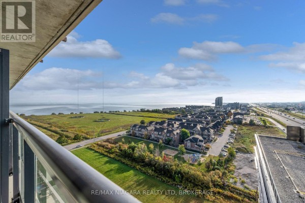 View from apartment balcony overlooking a grassy field, townhouses, and Lake Ontario. - 1307 - 550 North Service Road, Grimsby