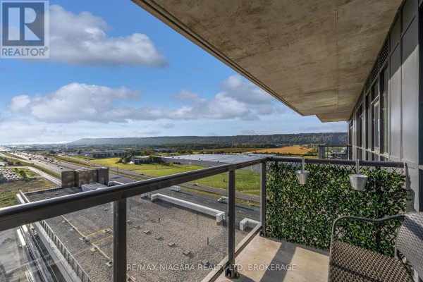 Balcony view of highway, industrial buildings, and rolling hills under a cloudy sky. - 1307 - 550 North Service Road, Grimsby