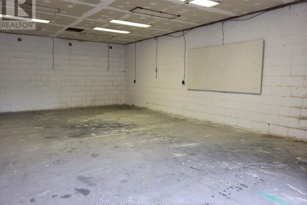 Corner view of an empty garage interior with concrete floor, cinder block walls, and pegboard. - 7 - 6029 Old Scugog Road, Clarington