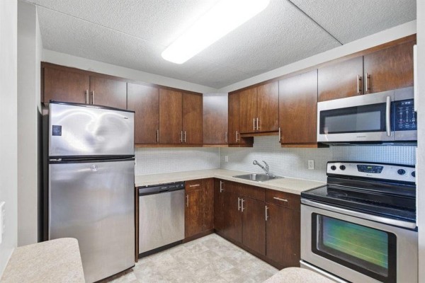 Kitchen with stainless steel appliances, dark wood cabinets, and light grey counters. - 7 134 Regis Drive, Winnipeg