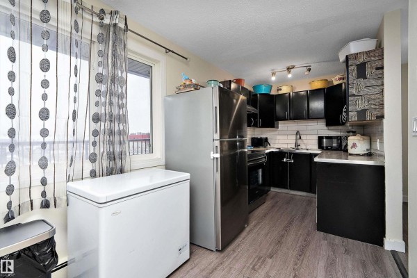 Bright kitchen area with large window, stainless steel fridge, and black cabinetry. - #7 13460 Fort Rd Nw, Edmonton