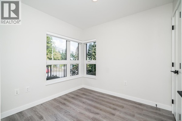Empty room with light grey walls, wood-look flooring, and large corner windows. - 7 50 Seaview Drive, Port Moody
