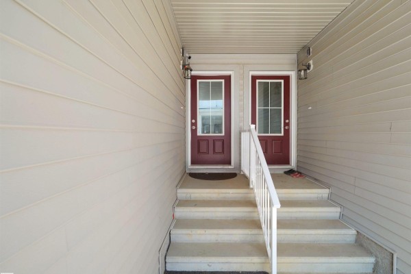 Two maroon front doors with glass panes, accessed by gray concrete stairs. - #7 7110 Keswick Common Sw, Edmonton