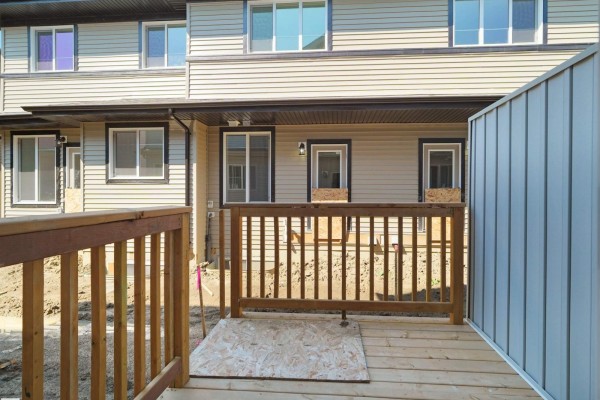 Wooden deck with railing in front of a townhouse with tan siding and windows. - #7 7110 Keswick Common Sw, Edmonton