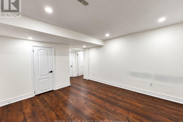 An empty unfinished basement room with white walls, wood floors, and recessed lighting. - 7 Aquilina Court, Ajax