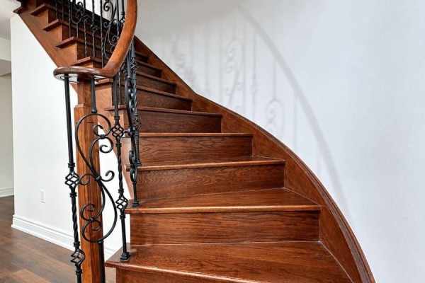 A close-up view of a curved wooden staircase with dark wood steps and black metal spindles. - 7 Aquilina Court, Ajax