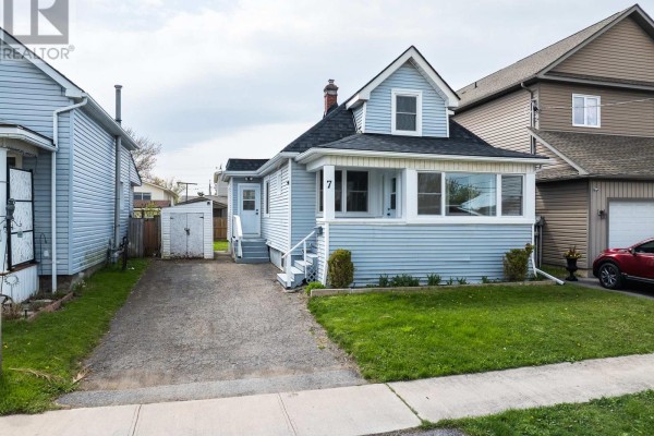 Front exterior view of a light blue sided house with a covered front porch and a gravel driveway. - 7 Battle Street, Thorold