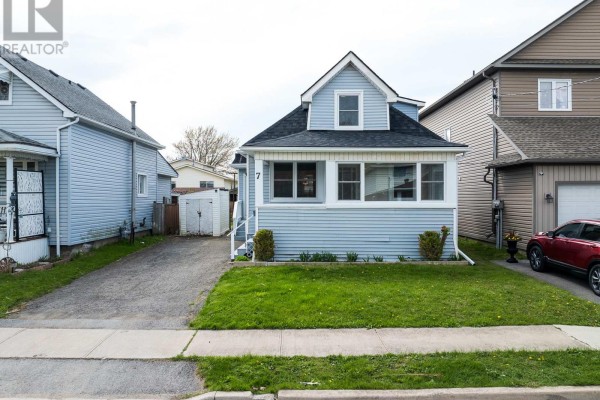 Front exterior view of a light blue sided house with a covered front porch and a gravel driveway. - 7 Battle Street, Thorold