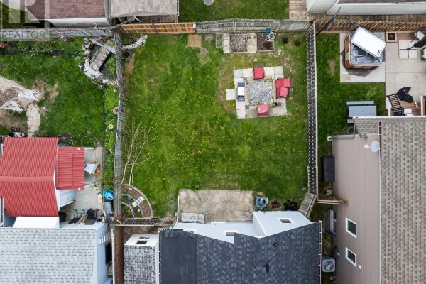 Aerial view of the fenced backyard showing a grass lawn, fire pit, hot tub, and patio furniture. - 7 Battle Street, Thorold