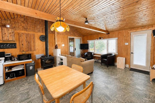 Open concept living and kitchen area with wood paneling, wood stove, and dining table. - 7 Block 4 Road, Betula Lake
