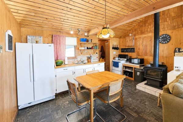 Kitchen with white appliances, wood cabinets, wood paneling, and a wood stove in the living area. - 7 Block 4 Road, Betula Lake