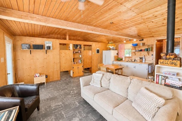 Spacious living room with wood paneling, sofa, armchairs, and a view into the kitchen area. - 7 Block 4 Road, Betula Lake