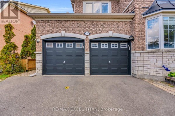 Close-up of a stone and brick home with two dark gray garage doors and decorative stone accents. - 7 Braydon Boulevard, Brampton