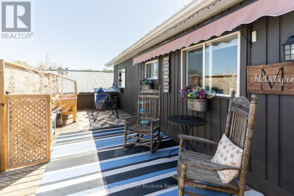 Deck with two rocking chairs, a table, and a barbecue on a sunny day. - 7 East Airport Road, Huntsville