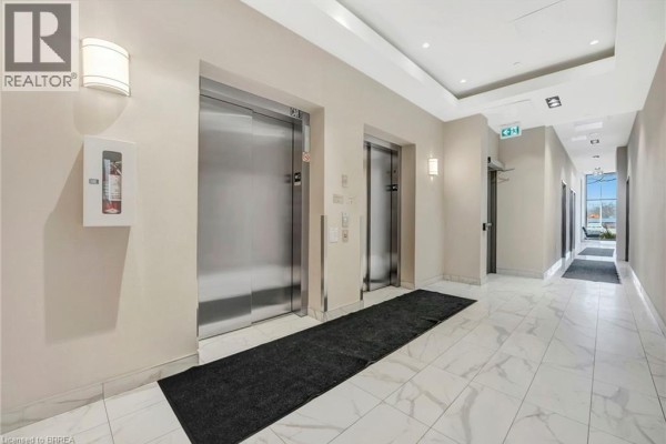 Apartment building hallway with two stainless steel elevators, sconce lighting, and marble tile flooring. - 7 Erie Avenue Unit# 813, Brantford