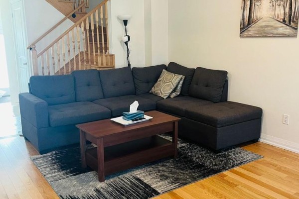 Living room with a dark sectional sofa, coffee table, rug, stairs, and artwork on the wall. - 7 Federica Crescent, Wasaga Beach