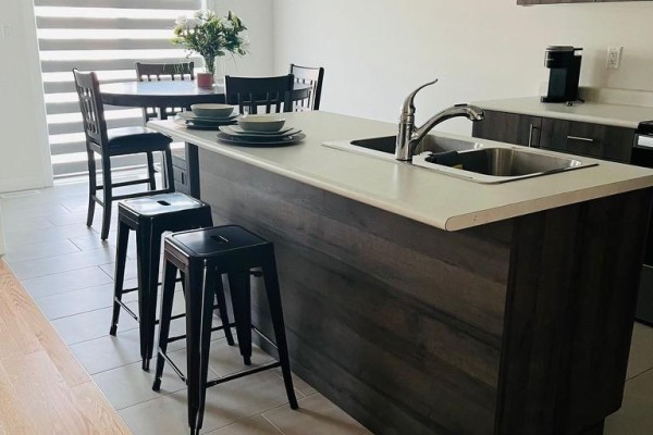 Kitchen island with a sink, faucet, and bar stools, next to a dining table and chairs. - 7 Federica Crescent, Wasaga Beach
